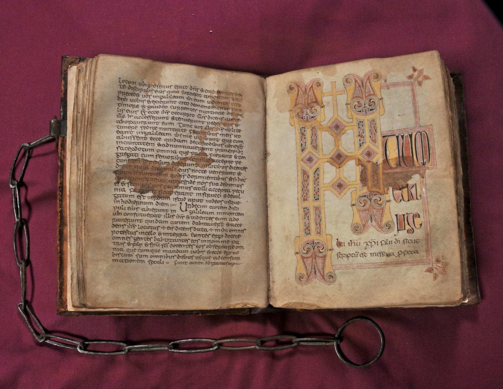 An open book with handwritten script on the left hand page and illustrations on the right. There is a chain attached to the spine of the book