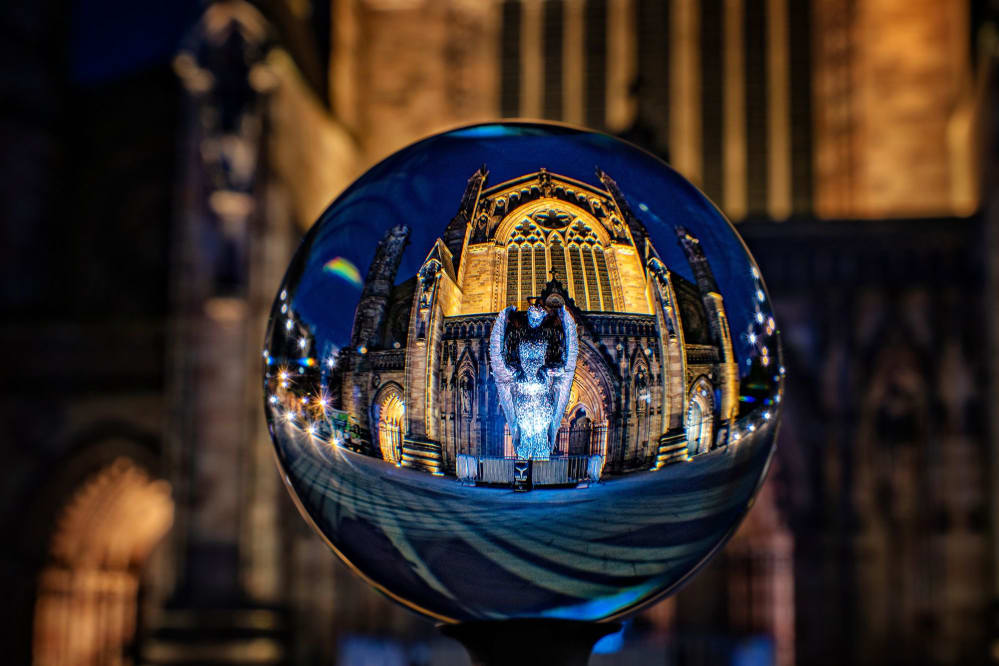 The Knife Angel is reflected in a glass ball which is held up in front of the cathedral at night time