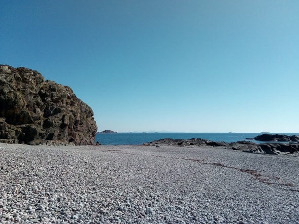 A photograph of a shingle beach taken in the sunshine looking out to sea