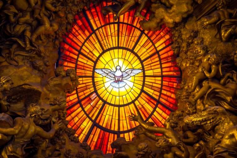A stained glass window. A dove is in the centre with orange and yellow glass radiating from around it