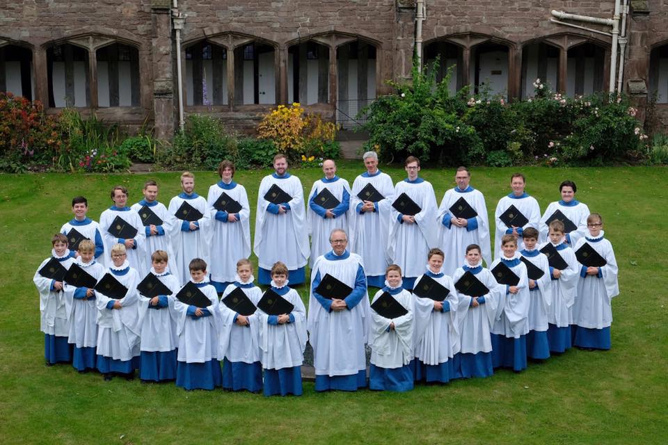 The cathedral choir in full robes stood in the cloisters. The photograph is taken from height looking down and choir is stood in a circle around the fountain