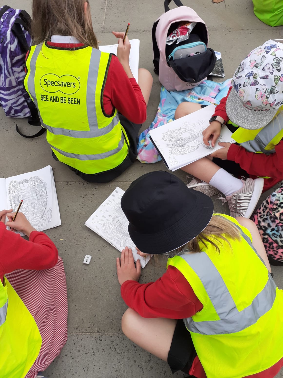A group of schoolchildren sit on the floor outside filling in worksheets