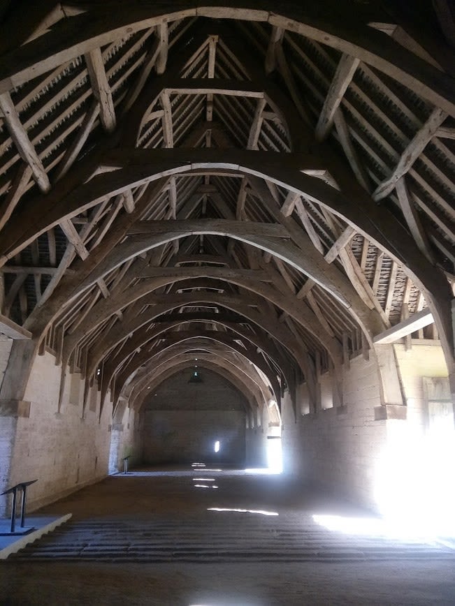 The interior of an empty medieval barn, there are wooden arches and light pouring in