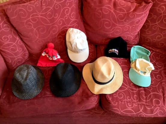 A selection of hats (straw hat, cap, bobble hat etc) are laid out onto a red sofa